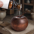 Decorative copper apple with a bottle pouring liquid onto it on a wooden surface.