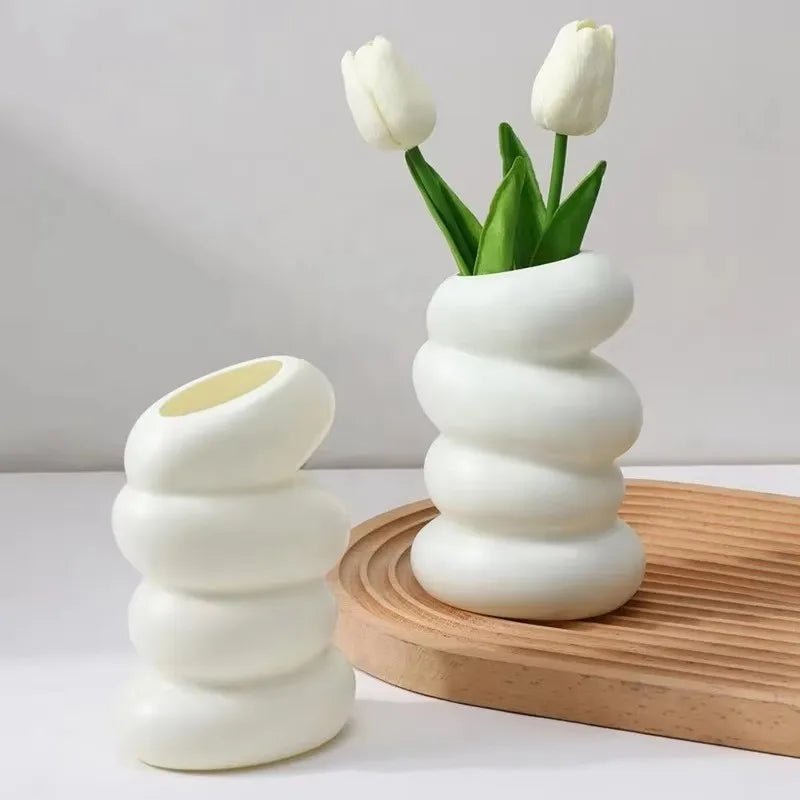 Two white ceramic vases with a textured design, one holding tulips, on a light background.