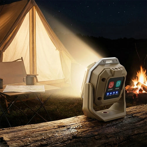 A portable projector lamp sits on a wooden log at night beside a lit campfire and a glowing tent, casting a bright beam of light toward the viewer. The device has a beige body with a small front display showing red and green icons.