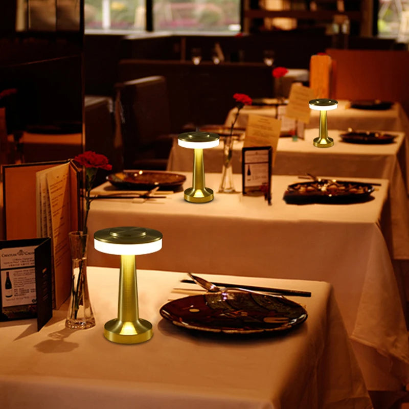 Dining tables set with white tablecloths, black plates, and small green lamps in a restaurant setting.