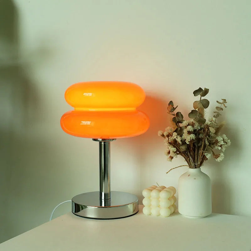 Orange table lamp on a white surface with a vase of flowers and a candle.