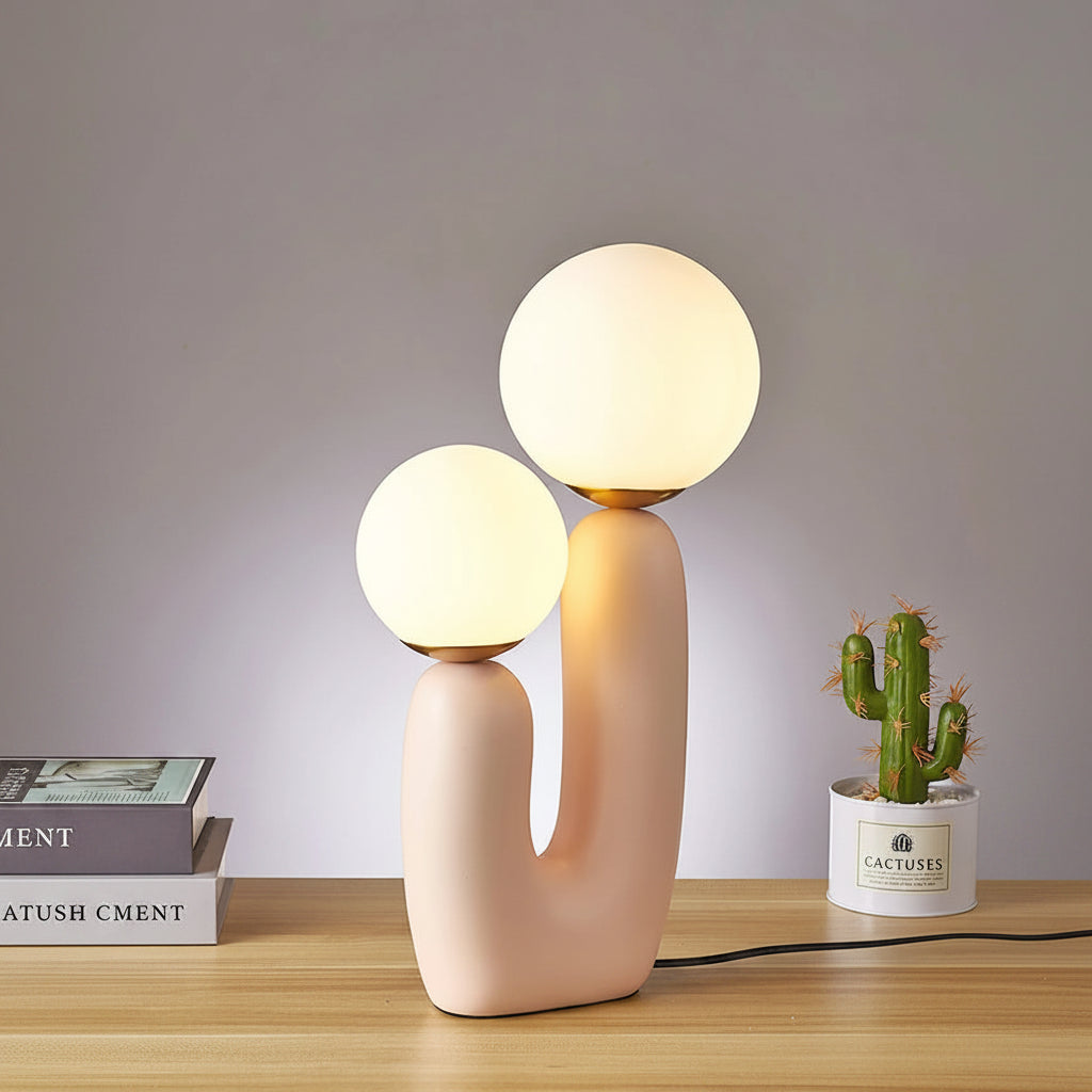 Modern table lamp with two spherical bulbs on a wooden surface, next to a cactus plant.