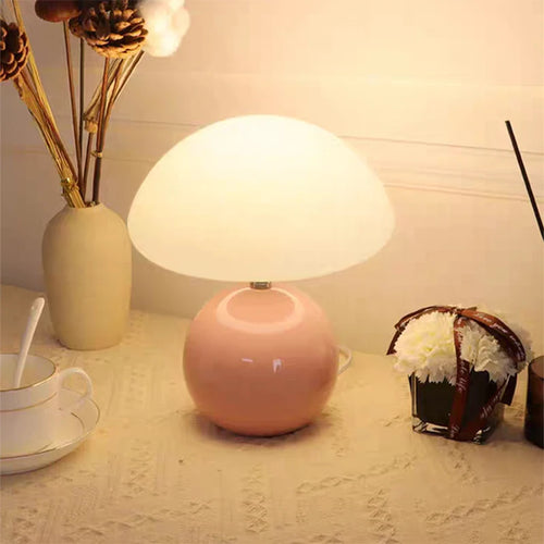Pink table lamp on a surface with a cup, saucer, and decorative items.
