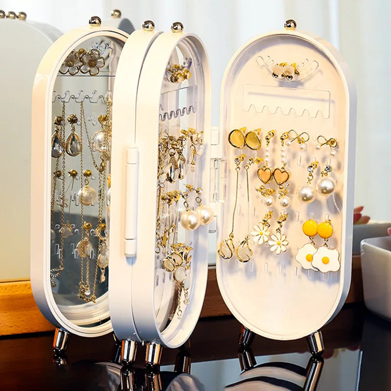 Three open jewelry organizers displaying necklaces and earrings on a table.