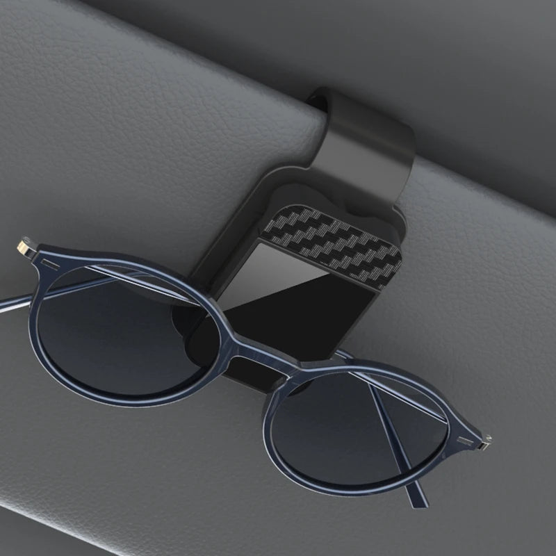 Blue eyeglasses on a car visor with a carbon fiber pattern clip.