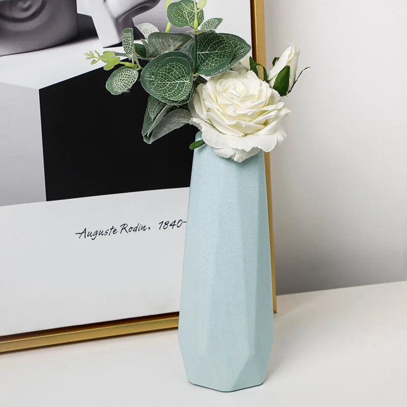 Light blue vase with white flowers and green leaves on a white surface