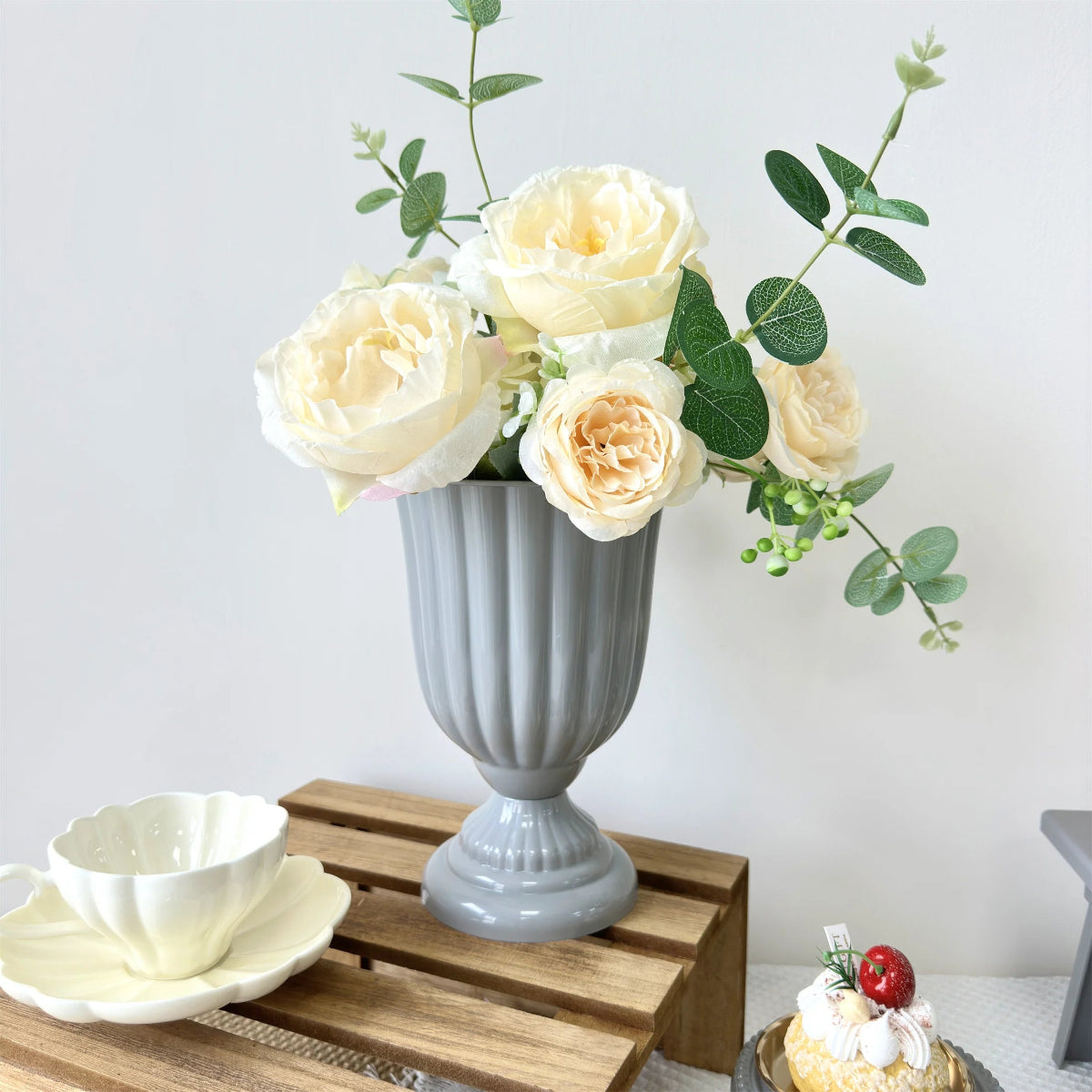 Gray urn vase with white flowers on a wooden crate against a white background
