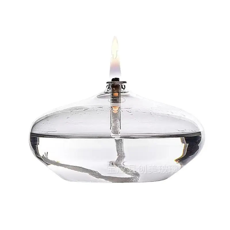Clear glass oil lamp with a lit wick on a white background