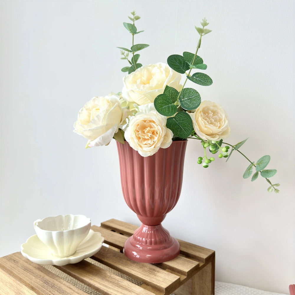 Pink vase with white flowers on a wooden table against a white wall