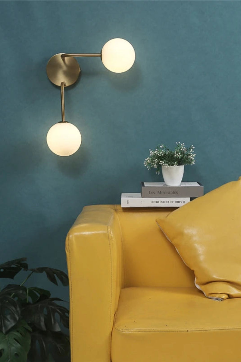 Yellow leather sofa with decorative pillows against a teal wall with two spherical wall lights.