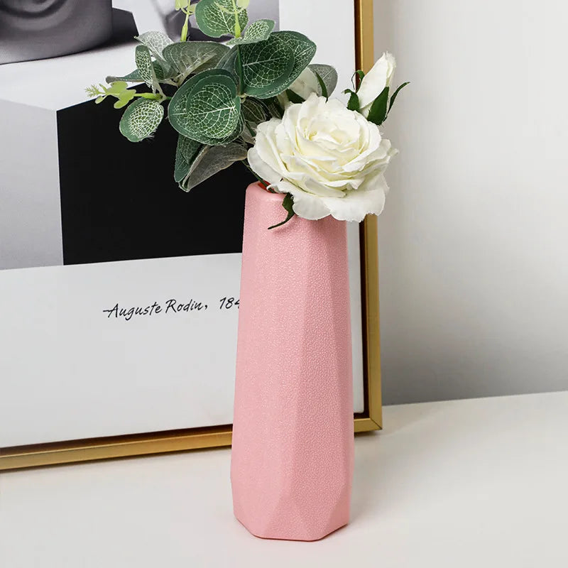 Pink vase with white flowers and green leaves on a white surface