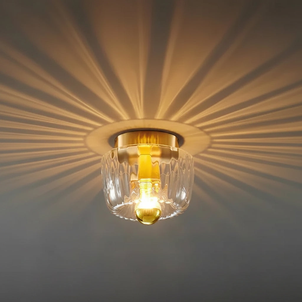 Ceiling light fixture with gold trim and clear glass shade on a neutral background